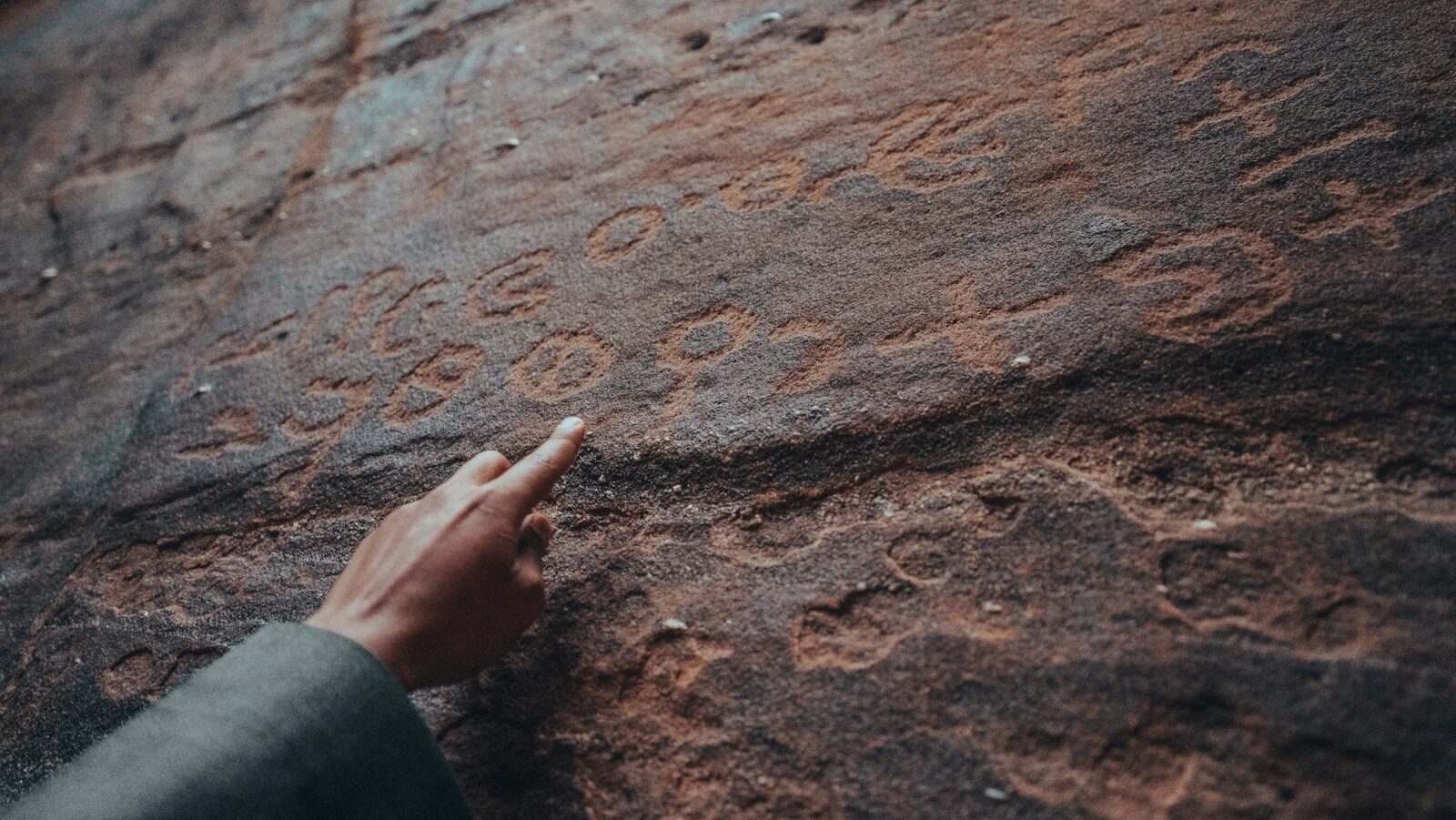 a person pointing at a rock with writing on it